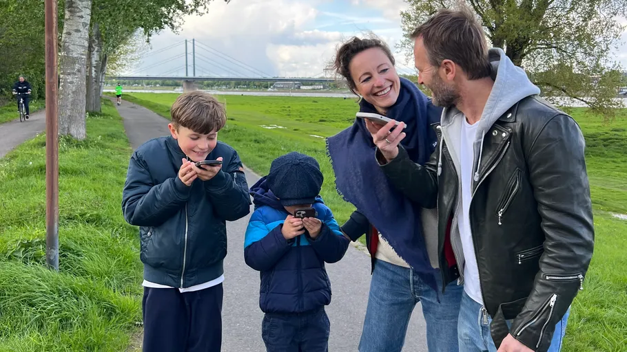 Family laughing while looking at phones in park.