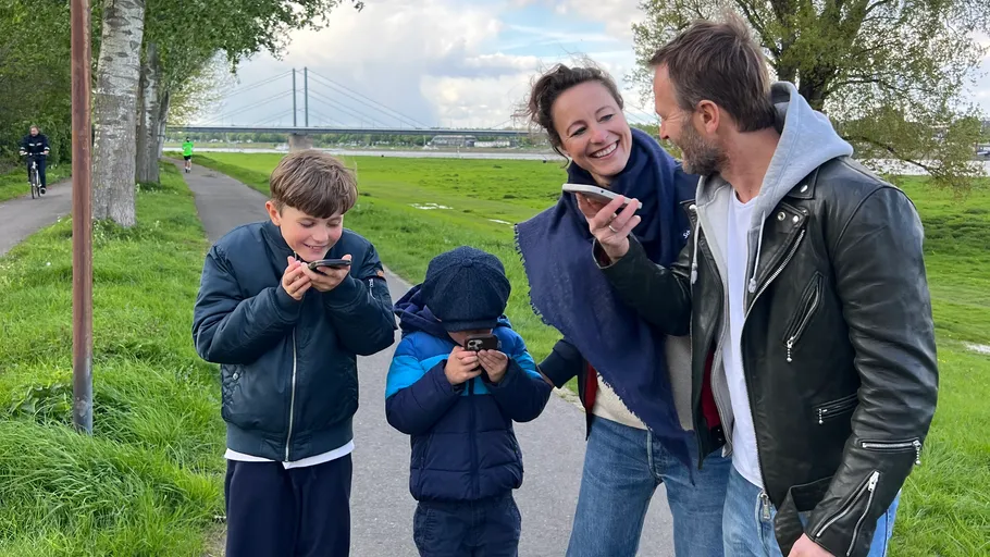 Family laughing, using phones in park.