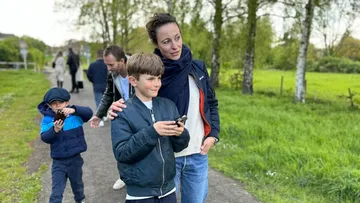 People walking on path with phones outdoors.