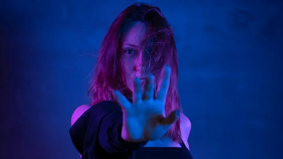 Woman reaches out under blue and pink lighting.