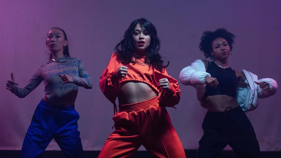 Three dancers performing on stage under purple lighting.