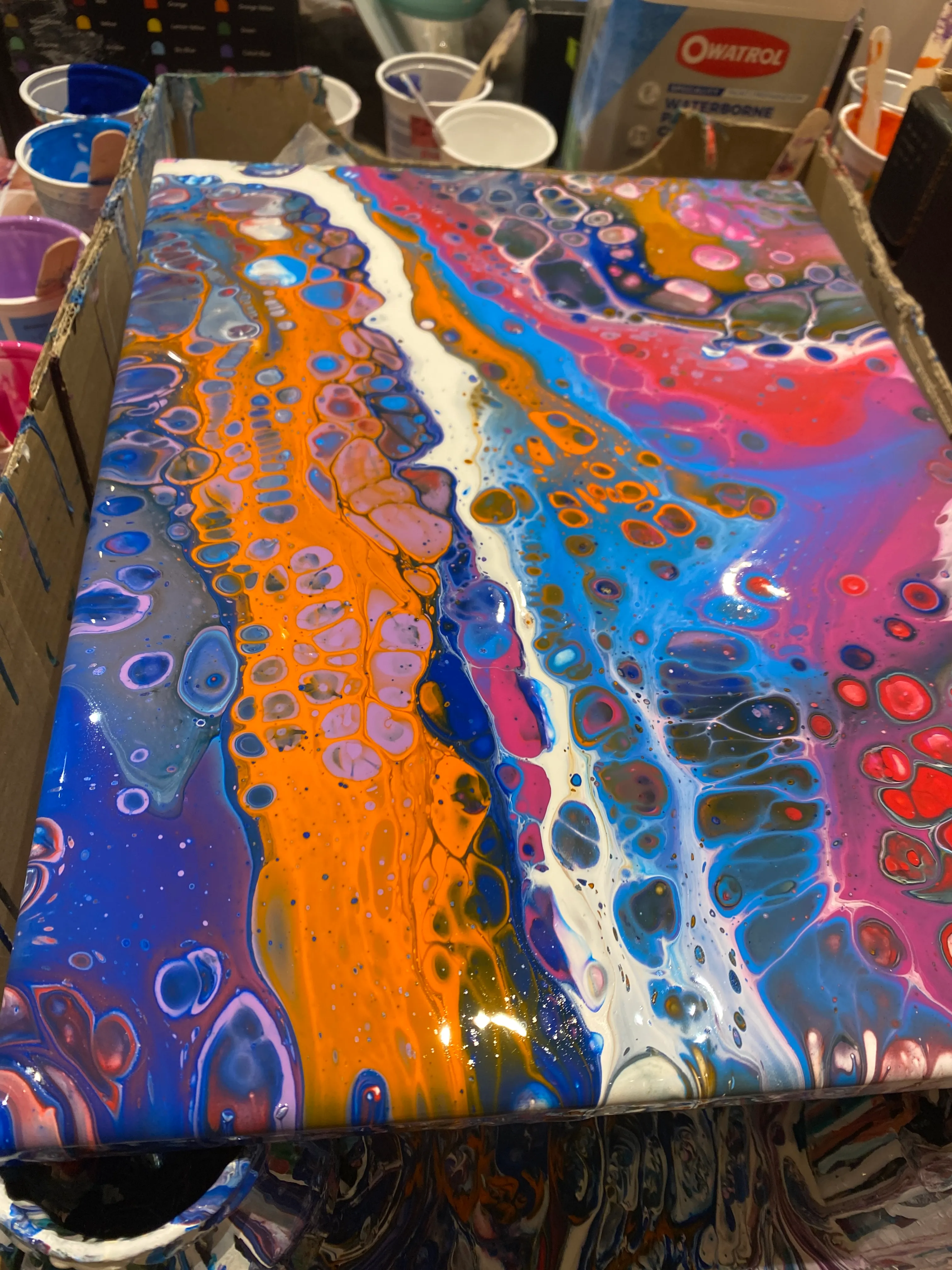 Buntes Farbgießen auf Leinwand mit Bechern daneben.
