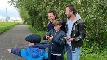 Family on path using phones, surrounded by trees.