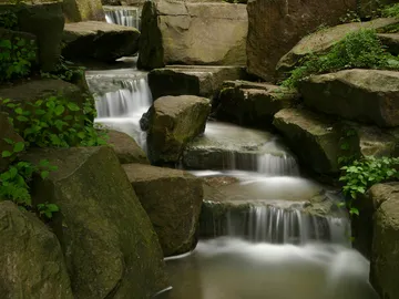 A waterfall flows gently between large stones.