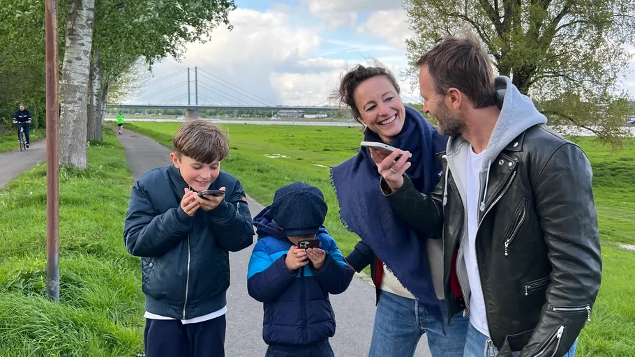 Family using smartphones on a riverside path.