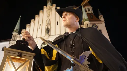 Man in historical costume holds lantern and sword.