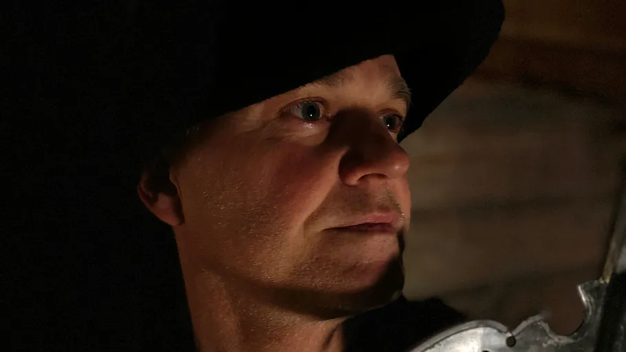 Mann mit Hut, schaut intensiv, schwaches Licht.