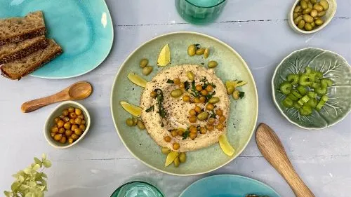 Hummus mit Kichererbsen und Gemüse auf einem Tisch.