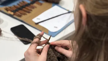 Person strickt mit Werkzeugen auf Tisch.