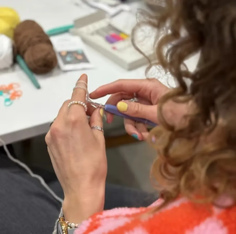 Person crocheting with yarn and tools on table.