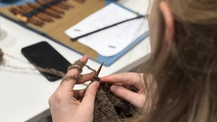 Person knitting with brown yarn, table background.