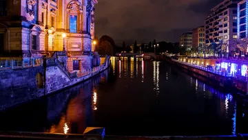Beleuchtetes Gebäude spiegelt sich nachts im Fluss.
