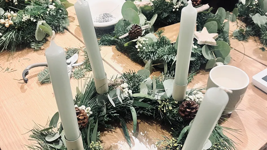 Green candles in holiday wreath on wooden table.