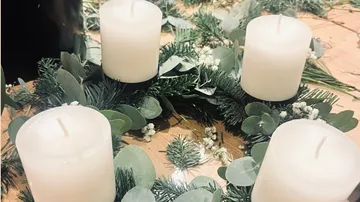Vier Kerzen auf einem grünen Kranz, Holztisch.