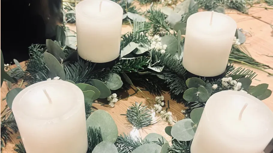 Four candles on a greenery wreath, wooden table.