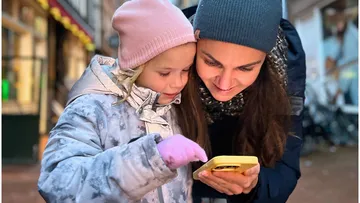 Kind und Erwachsene lächeln beim Handy schauen.