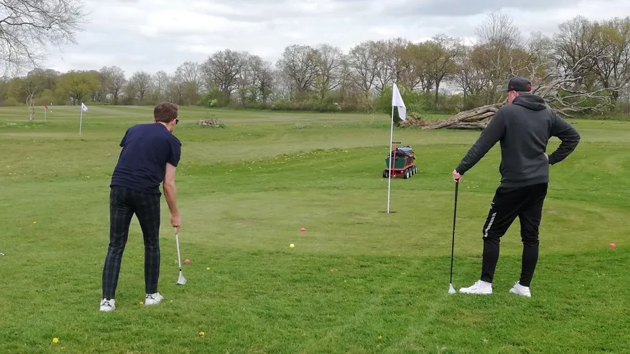 Zwei Männer spielen Golf auf grünem Feld.