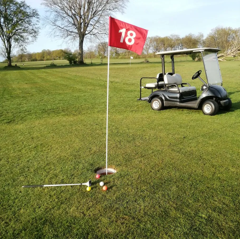Golfwagen parkt neben Loch achtzehn.