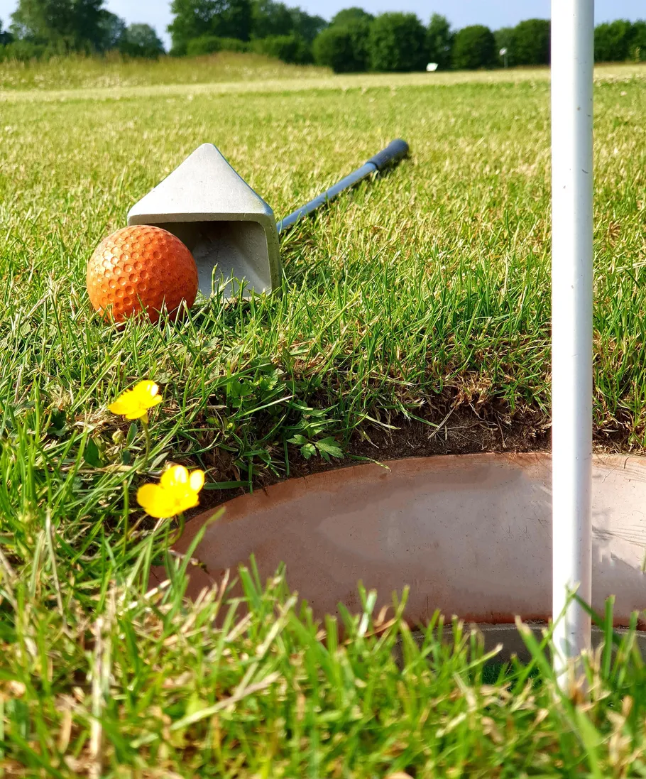 Minigolf-Ausrüstung auf grasigem Platz nahe Loch.