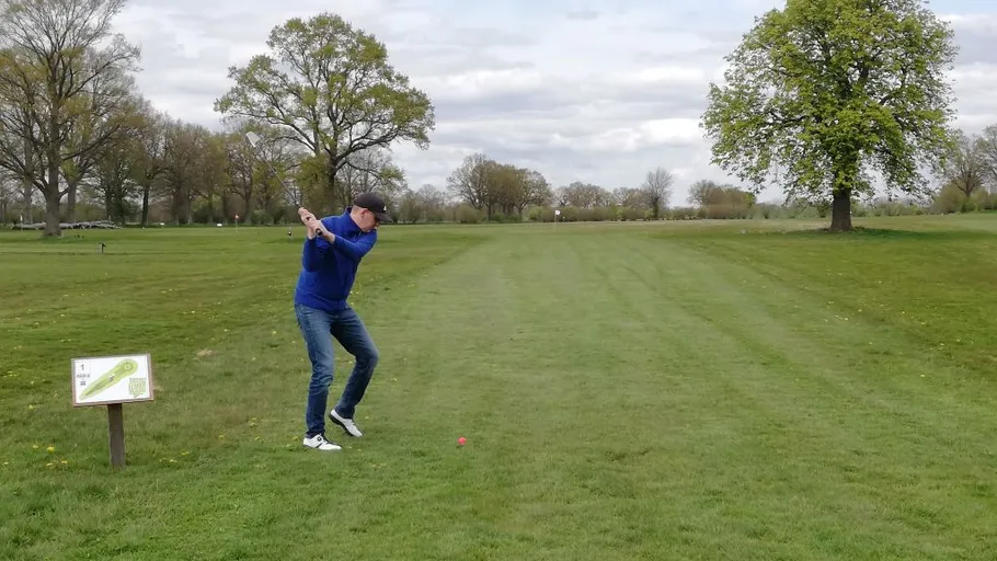Golfer swinging club on lush green course.