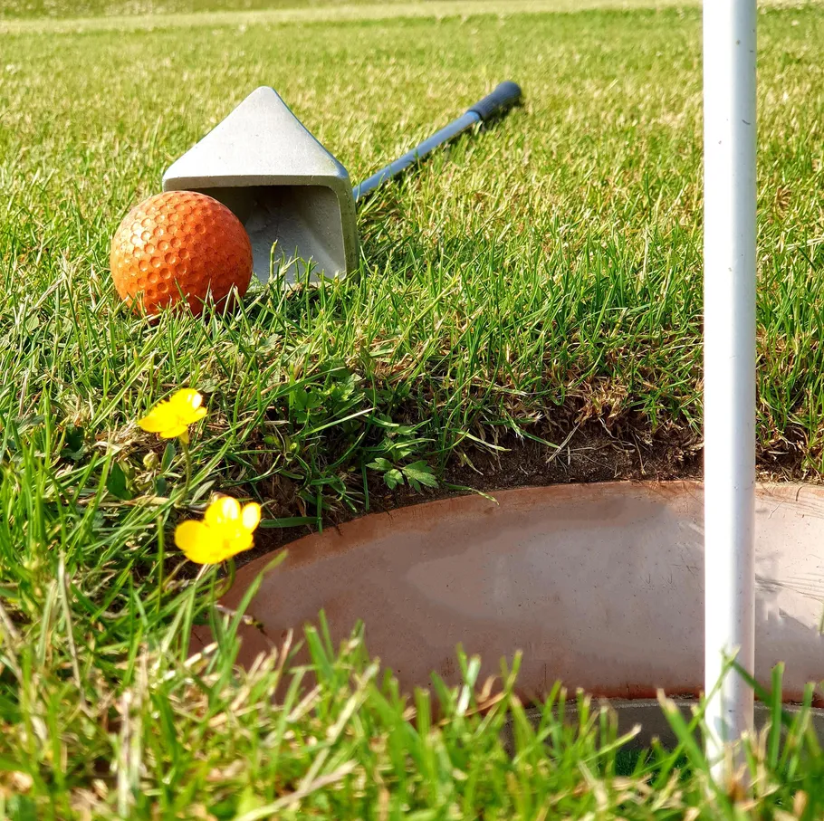 Golfschläger, Ball nahe Loch auf Gras.