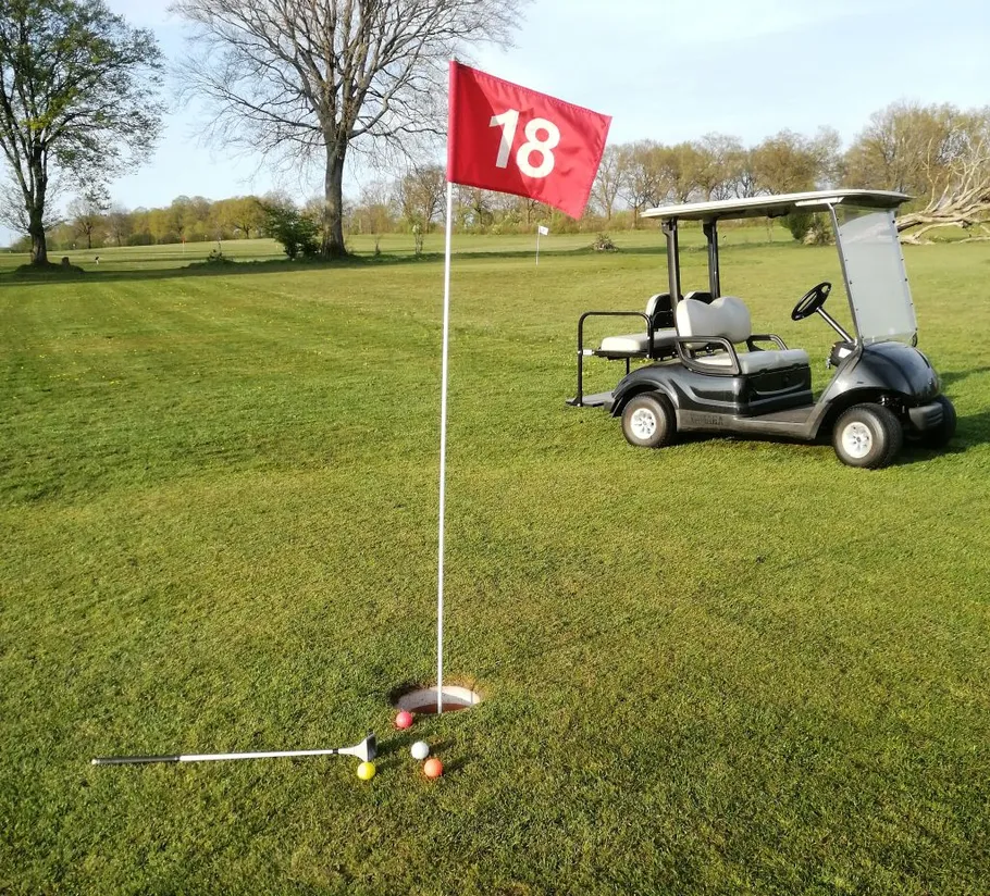 Golfbälle nahe Loch, rote Fahne, Golfwagen.