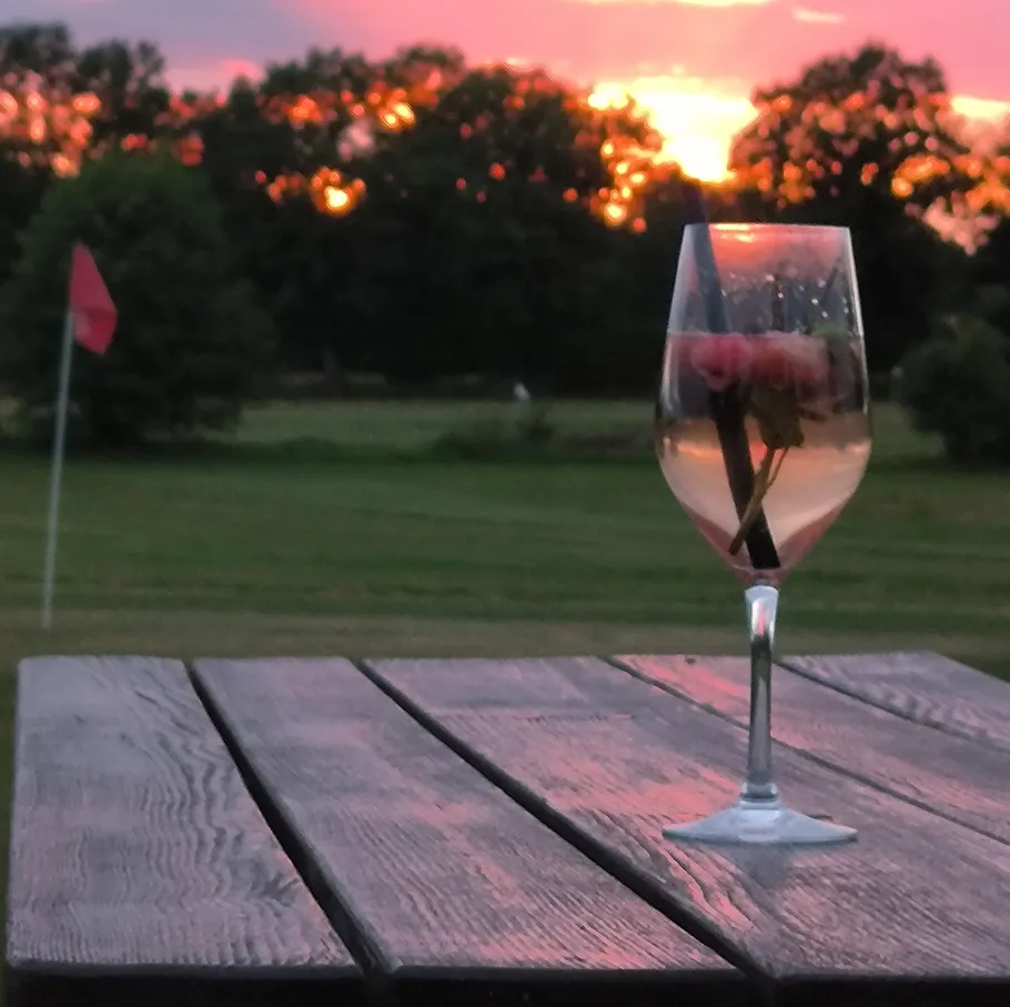 Weinglas mit Blumen auf Tisch, Sonnenuntergang Hintergrund.