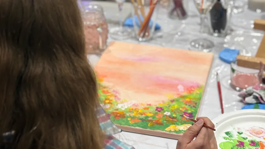 Person painting colorful floral canvas at table.