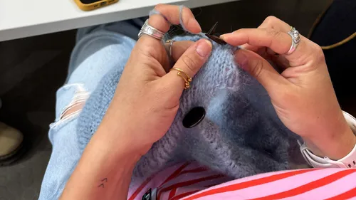 Person knitting blue fabric while seated.