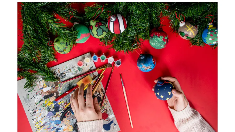 Person malt Weihnachtskugeln auf dem Tisch.