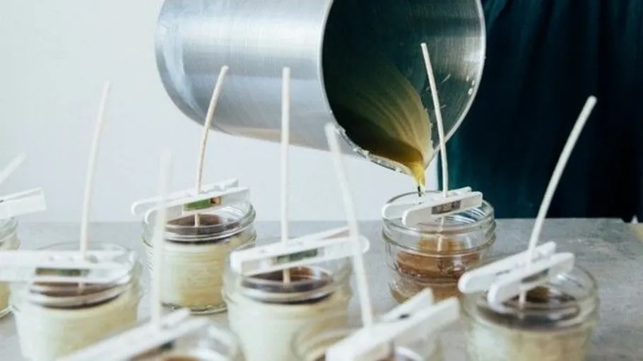 Person gießt Wachs in Glaskerzenbehälter.