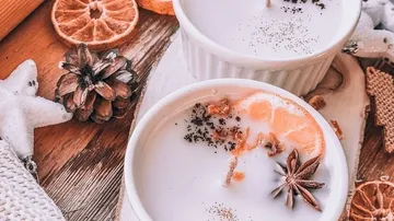 Tassen mit gewürzter Milch, Sternanis und Zitrusfrüchten.