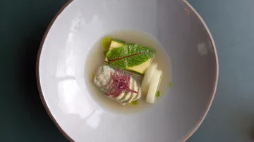 Elegantes Gericht mit Gemüse in Brühe auf Teller.