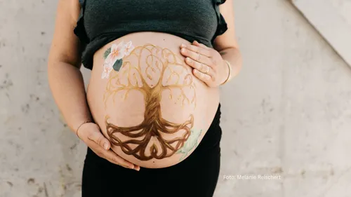 Schwangerenbauch mit Baumgemälde, Hände berühren.