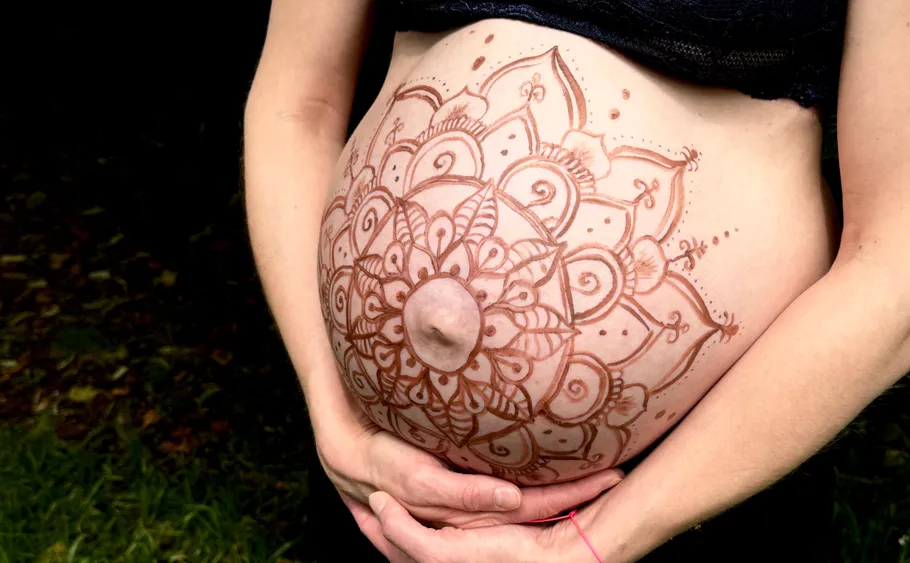 Pregnant belly with henna design outdoors.