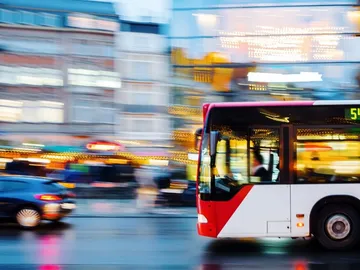 Ein Bus fährt schnell durch eine beleuchtete Stadtstraße.