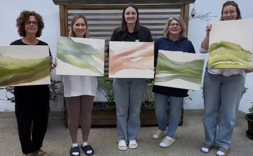 Five women holding paintings outdoors.
