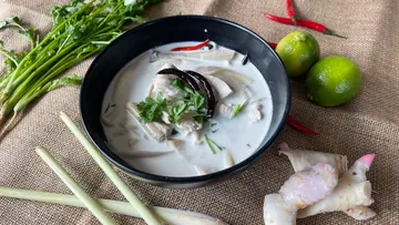 Chicken coconut soup in a black bowl with herbs.