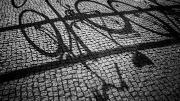 Bicycle shadows cast on cobblestone pavement.