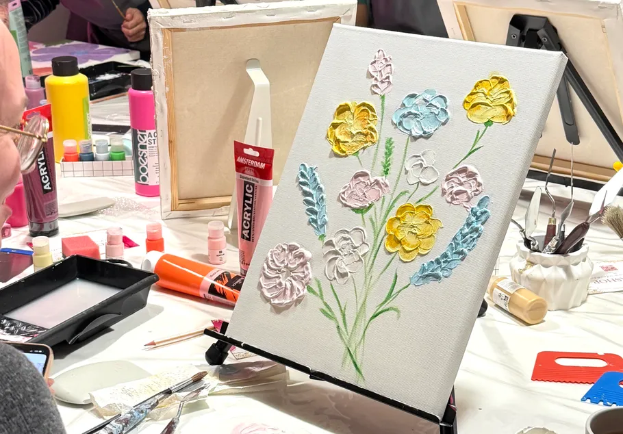 Canvas with colorful flowers being painted, art supplies nearby.