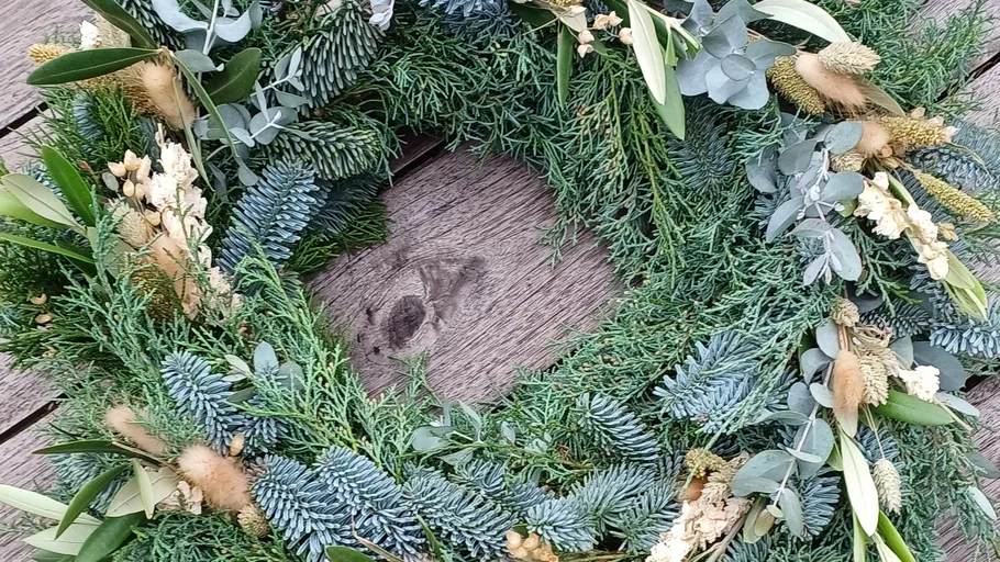 Green wreath with dried flowers on wood.