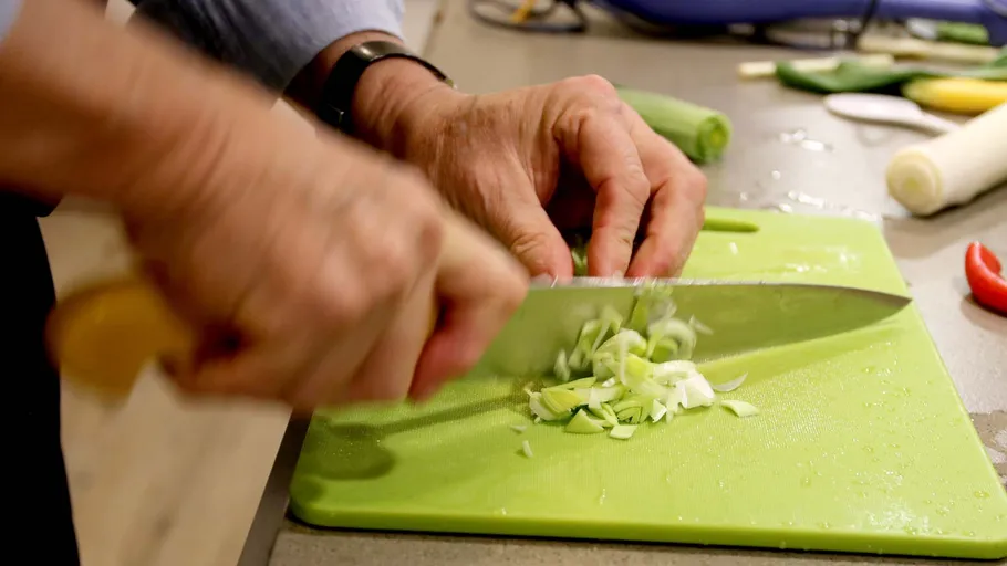 Hands chopping vegetables on green board.