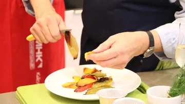 Person richtet gegrilltes Gemüse auf Teller an.
