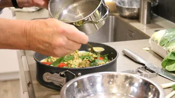 Person seasoning food in kitchen pan.