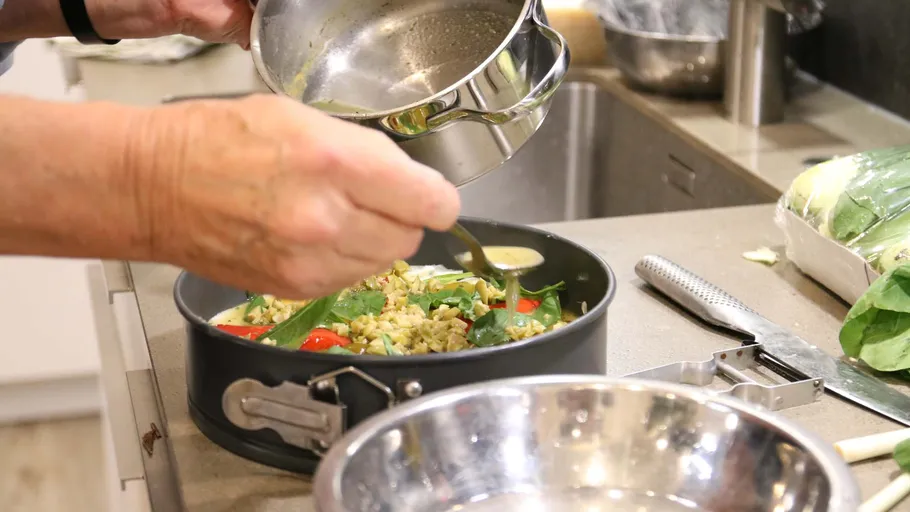 Person würzt Essen in Küchenpfanne.