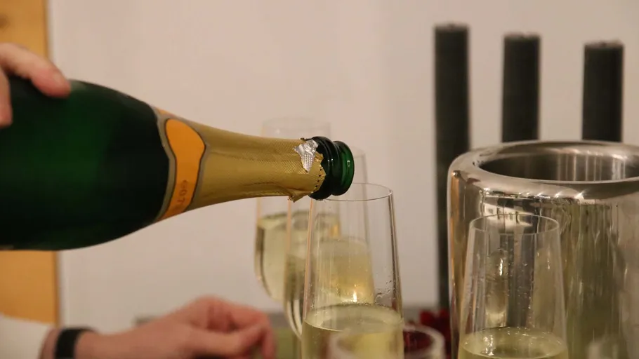 Champagne bottle pouring into glass, indoor setting.