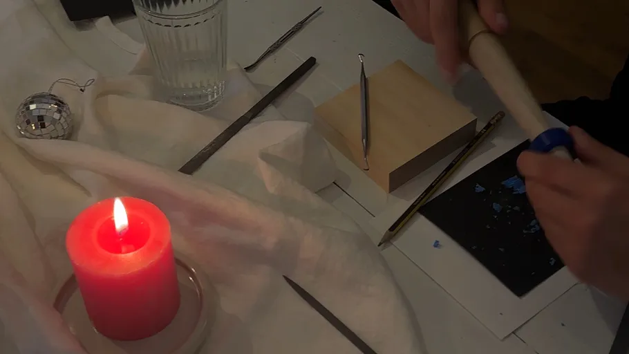 Person crafting on table with candle nearby.