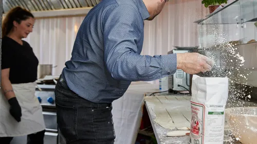 Chef sprinkling flour in busy kitchen.
