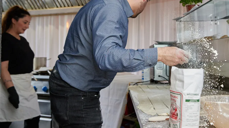 Chef sprinkling flour in busy kitchen.