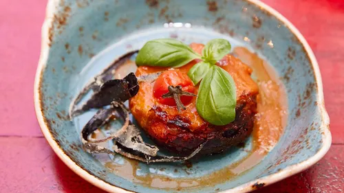 Gourmet dish with tomato, basil garnish, turquoise plate.